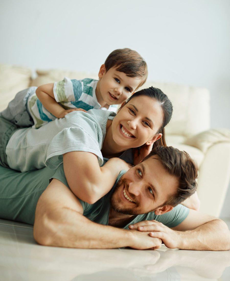 Happy family making human pyramid on the floor at home and looking at camera.