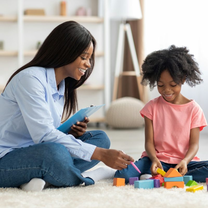 Adorable black kid and child psychotherapist playing with bricks